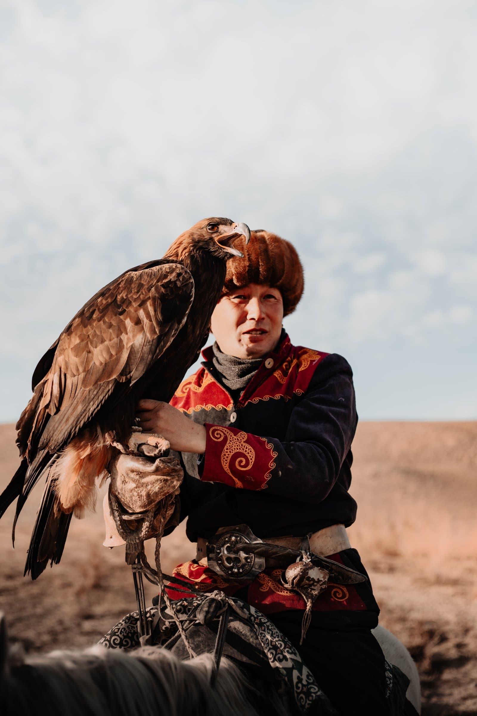 An eagle hunter on horseback holding his golden eagle