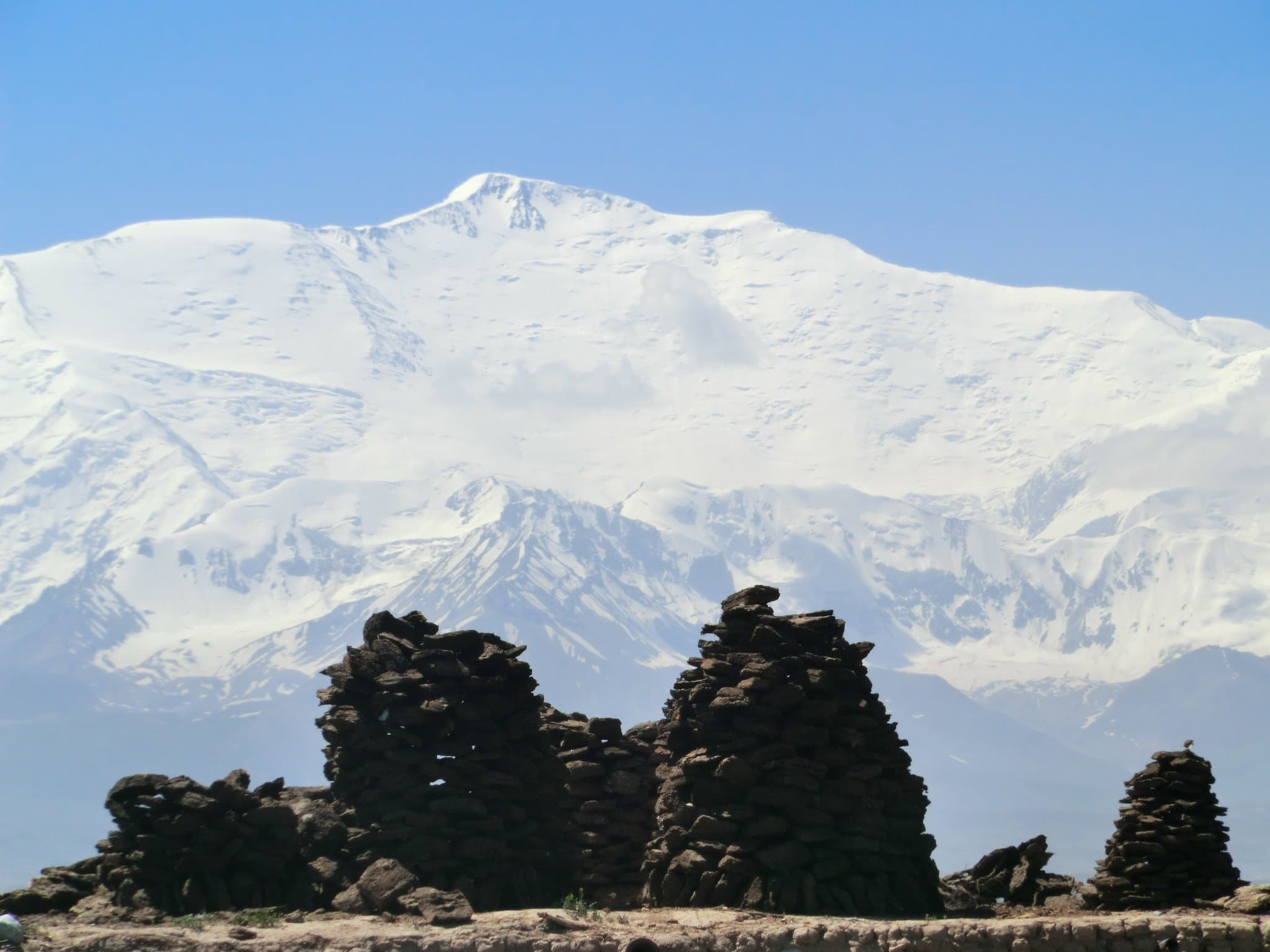 Snow-covered Lenin Peak rising above stone cairns at Achik-Tash